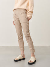 Afbeelding in Gallery-weergave laden, Zandkleurige Broek van Jane Lushka, Doris Pants van de travel kwaliteit zit uiterst comfortabel, een slim fit broek met veel stretch. Deze broek heeft een elastische band, grote zakken op de voorkant, een prachtig design, waardoor de broek een combi is van minimalistisch cargo en chic casual. Op de achterkant heeft de broek zakken met knoopjes.