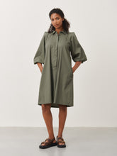 Afbeelding in Gallery-weergave laden, Groene Jurk Carlen ES92421115 van Jane Lushka is een sportieve korte wijde jurk van katoen met kraag en bedekte knoopjes tot halverwege jurk. Jurk heeft 3/4 pofmouwen met elastiek en steekzakken aan beide kanten. Deze jurk heeft geen lusjes, maar wel een lange ceintuur in dezelfde stof voor een nonchalant effect, ook zonder ceintuur te dragen. De Carlen Jurk draagt erg comfortabel door het soepele katoen en is goed te dragen voor elke gelegenheid. Het model is 1,79 cm lang en draagt maat S.