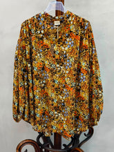 Load image into Gallery viewer, Oversized blouse met lange mouwen, een V-hals en elastieken manchetten. Deze luchtige blouse van katoen is translucent en heeft een okergele basis met contrasterende kleuren in bloemmotief. De achterkant valt langer dan de voorkant, wat zorgt voor een speels en modern silhouet. Perfect voor een casual maar trendy look.