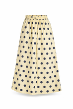 Load image into Gallery viewer, Maxi Rok Norma is een elegante, zachtgele lange rok met speelse donkerblauwe stippen. De rok heeft een comfortabele elastische tailleband, waardoor hij mooi aansluit en prettig draagt. Dankzij de praktische steekzakken combineert Rok Norma stijl met gemak, perfect voor zowel een casual als een meer geklede look.