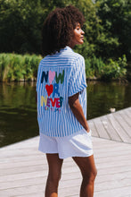 Afbeelding in Gallery-weergave laden, Gestreepte Blouse Now or Never Wit is een zomerse blouse van 100% katoen met korte mouwen en kraag. De voorkant van deze blouse heeft een rood hart en de achterkant is voorzien van een kleurrijke opdruk 'Now or Never'.