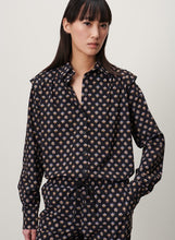 Afbeelding in Gallery-weergave laden, Blouse Hanna is een zwarte blouse met mooi bloemmotief, uit de collectie van Jane Lushka. Hanna blouse heeft plooitjes, lange mouwen met manchetten en dubbele knoopjes, subtiele ruches op de schouders en een klassieke kraag. Deze prachtige blouse is ook ontzettend mooi om te dragen op een donkere broek, onder een pak, gilet of vest. De blouse is van de bekende travel kwaliteit en is verkrijgbaar in verschillende maten.