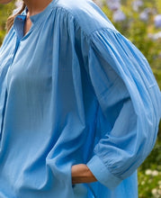 Load image into Gallery viewer, Blauwe Blouse Jasmin van de Moment Amsterdam Collectie is een wijde translucent blouse met een ronde hals, lange mouwen met plooitjes en bedekte knoopjes. Deze moderne blouse is een klokkend model met plooitjes. Een fijne blouse die je heerlijk door kunt dragen.