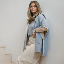Afbeelding in Gallery-weergave laden, Deze poncho van Cycleur de Luxe biedt zowel stijl als sportiviteit. Deze poncho heeft lichtblauw als basiskleur met grijze accenten en is vervaardigd van een luxe mix. Met een eigentijdse capuchon en boeiende kleurvlakken aan de binnenkant zet poncho LAURA de trend. Deze cape poncho zorgt voor ongeëvenaard comfort en een lange levensduur en toont de kunst van de mondiale mode. Ontdek de perfecte aanvulling op jouw garderobe, is perfect te combineren met de prachtige LENA trui.