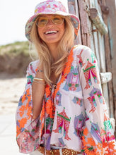 Afbeelding in Gallery-weergave laden, Witte Top, Tents Wide Sleeves van Place du Soleil. De blouse is een klokkend model, heeft wijde trompetmouwen met prachtig fluo oranje embroiderie en pailletten. Deze geweldige blouse is gevoerd, heeft een diepe V-hals met strikdetail en fluo oranje flosjes. Op deze top zijn afbeeldingen te zien van circustenten, in een prachtige oudroze kleur in combinatie met groen, blauw, oranje en roze.