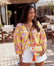 Afbeelding in Gallery-weergave laden, Gele Blouse Yellow Print Purple Embroidery van Place du Soleil. De blouse is een licht klokkend model met 3/4 mouwen met manchet en heeft werkelijk prachtige borduursels in paars en oranje met pailletten. Blouse top heeft 4 knoopjes en strikkoord met oranje flosjes. Deze geweldige blouse is in de kleurencombinatie geel, paars, oranje.