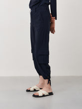 Afbeelding in Gallery-weergave laden, Blauwe Broek in Travelkwaliteit, Trend Pants U2242024 van Jane Lushka Collectie is een mooie lange nette cargo broek met een rechte losse pijp en strikje onderaan de broek voor een subtiele pof. Trend Broek heeft lusjes voor een ceintuur en een rits en knoop om de broek te sluiten en heeft aan een kant een klepzak en is van de bekende travel kwaliteit.