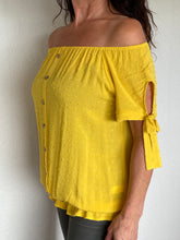 Afbeelding in Gallery-weergave laden, Gele Top Dobby heeft een kort mouwtje met een strikje, wat een leuk detail is. De top heeft een ronde hals, een rij knoopjes en heeft aan de onderzijde een elastische band met ruffles. Top kan zowel op de schouder als off-shoulder gedragen worden en is verkrijgbaar in verschillende kleuren. Kleur : Blauw, Geel, Wit