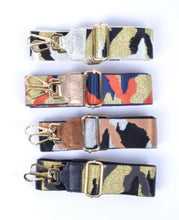 Afbeelding in Gallery-weergave laden, Bagstrap, schouderband voor aan een tas met trendy legerprint. Deze schouderband heeft een lederen uiteinde in de kleur zwart. De band is 5cm breed en is verstelbaar in de lengte. Minimale lengte , inclusief clips, is 84cm en de maximale lengte, inclusief clips is 125cm. De schouderband Leger is in verschillende kleuren verkrijgbaar: oranje/blauw/goud, zwart/grijs/goud en zwart/wit/goud.