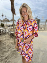 Load image into Gallery viewer, Jurk van Place du Soleil, Retro Fish is een prachtig kleurrijk middellang iets uitlopend model jurk met knoopjes en steekzakken, 3/4 mouwen met elastiek en een ronde kraag, die afgewerkt is met paarse band. De jurk heeft een onderjurk, is een mooi kleurenpalet en heeft een retro print. De jurk heeft een losse ceintuur in dezelfde print met gekleurde flosjes.