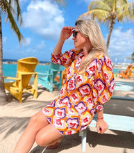 Load image into Gallery viewer, Jurk van Place du Soleil, Retro Fish is een prachtig kleurrijk middellang iets uitlopend model jurk met knoopjes en steekzakken, 3/4 mouwen met elastiek en een ronde kraag, die afgewerkt is met paarse band. De jurk heeft een onderjurk, is een mooi kleurenpalet en heeft een retro print. De jurk heeft een losse ceintuur in dezelfde print met gekleurde flosjes.