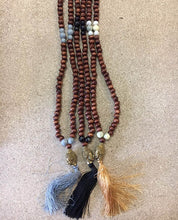 Load image into Gallery viewer, Ketting van Hot Lava is een mooie ketting met bruine kraaltjes en een aantal contrasterende kraaltjes, een buddha gezicht en een gekleurde franje in verschillende kleuren.

