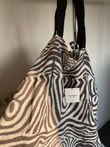 Zomerjurk, Kaftan van Moment by Moment in een vale zwart/wit print in zebra dessin. Zomerjurk heeft een ronde hals met vier knoopjes en heeft steekzakken. In deze serie is verkrijgbaar: Zomerjurk, super grote strandtas, te sluiten met een strikje en een mini tasje met rits.  Met deze prachtige set ben je helemaal klaar voor het strand of het terras. De kaftan/zomerjurk is ook los verkrijgbaar.