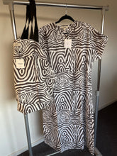 Load image into Gallery viewer, Zomerjurk, Kaftan van Moment by Moment in een vale zwart/wit print in zebra dessin. Zomerjurk heeft een ronde hals met vier knoopjes en heeft steekzakken. In deze serie is verkrijgbaar: Zomerjurk, super grote strandtas, te sluiten met een strikje en een mini tasje met rits.  Met deze prachtige set ben je helemaal klaar voor het strand of het terras. De kaftan/zomerjurk is ook los verkrijgbaar.
