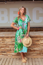 Afbeelding in Gallery-weergave laden, Groene Jurk van Place du Soleil, Green Jungle Dress is een prachtige lange zomerjurk met steekzakken, korte gerimpelde mouwen en V-hals, afgewerkt met roze franjes en gekleurde strik en flosjes. De jurk heeft een geweldige jungle print in de kleurcombinatie groen met turquoise. Wauw, een ware eyecatcher, deze jungle jurk!
