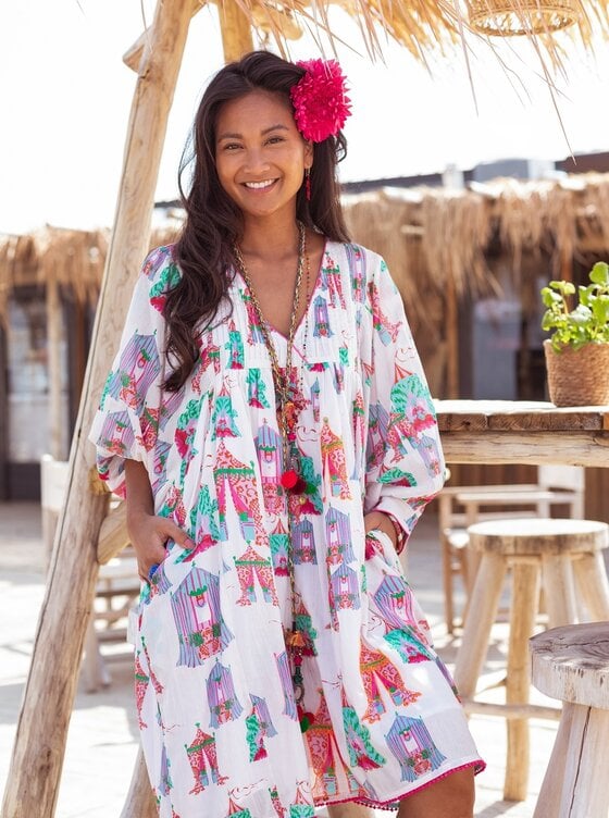 Witte Midi Jurk, Dress Tents Short van Place du Soleil. De Jurk is een ruimvallend klokkend model met steekzakken, heeft 3/4 mouwen, manchet met knoopje en een diepe V-hals, die afgewerkt is met een roze bies.