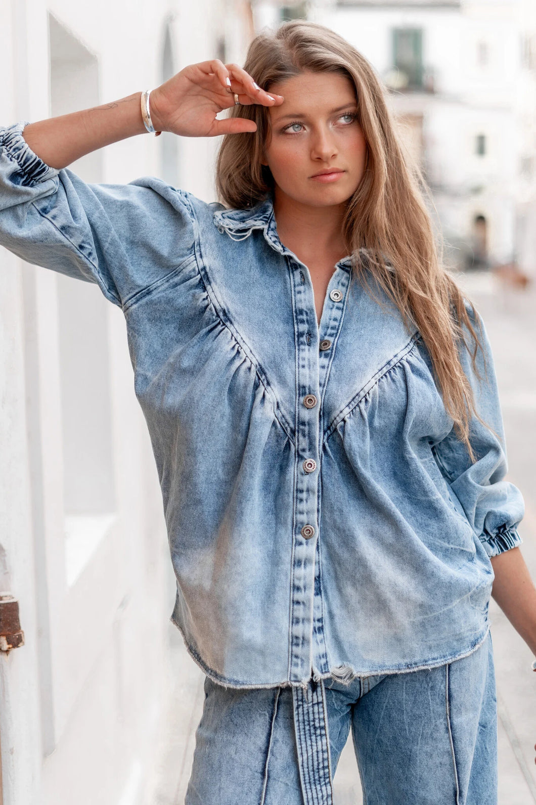 Denim Blouse Pancha Blue van ibzmode heeft een kraagje, sluit met de knopen, heeft gerafelde afwerkingen, elastiek bij de polsen en is geplooid bij de borsten. De gerafelde afwerkingen en elastiek bij de polsen geven een speelse twist aan het klassieke ontwerp. Verkrijgbaar in verschillende kleuren: Off White, Blue.