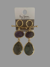 Load image into Gallery viewer, Goudkleurige Oorbellen Beauty Curl van by Jam, type oor stekers. Prachtige hangers, in de kleuren paars en groen. Een ware eyecatcher zijn deze statement oorbellen. Afmetingen van deze oorbellen: 6cm x 2cm.
