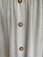 Load image into Gallery viewer, Witte Top Dobby heeft een kort mouwtje met een strikje, wat een leuk detail is. De top heeft een ronde hals, een rij knoopjes en heeft aan de onderzijde een elastische band met ruffles. Top kan zowel op de schouder als off-shoulder gedragen worden en is verkrijgbaar in verschillende kleuren.  Kleur : Blauw, Geel, Wit
