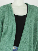 Load image into Gallery viewer, Groen Vest Suze is een royaal vallend grof gebreid vest met stoer uiterlijk en heeft franjes op het achterpand. Vest Suze is verkrijgbaar in verschillende kleuren: Emerald, Licht Beige, Zwart, one size en draagbaar t/m maat 42.
